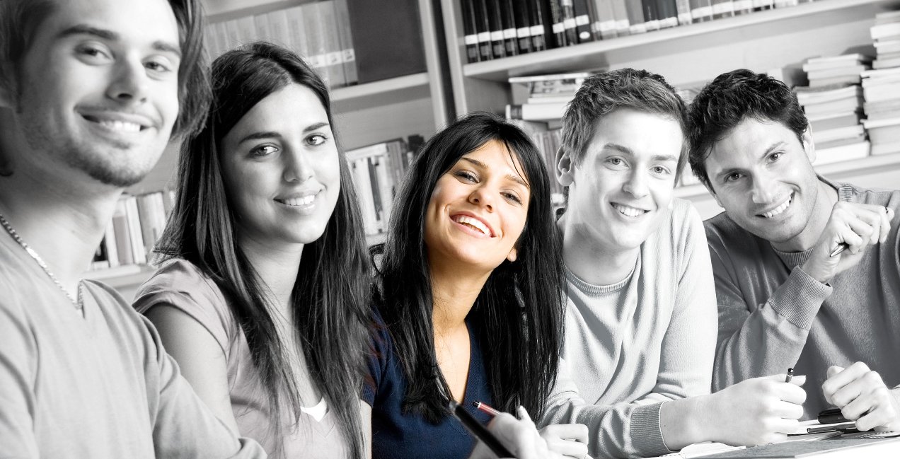 Fünf junge Studenten sitzen an einem Tisch und strahlen lachend in die Kamera.